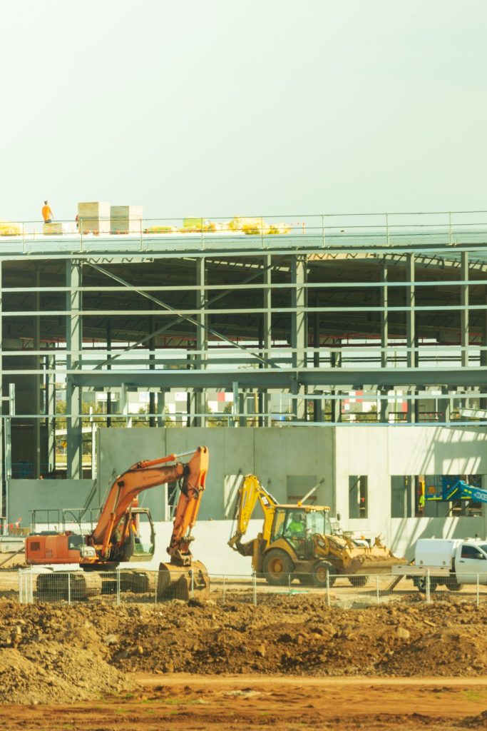 Steel-frame building under construction with excavators on site
